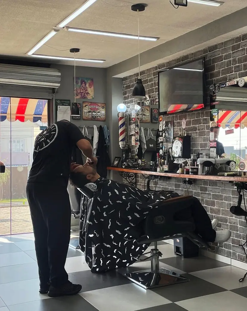 Barba feita com o cliente reclinado na cadeira, ao lado do poste de barbeiro