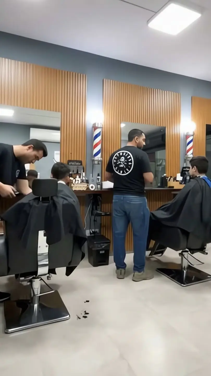Salão da Barbearia Barão: painéis de madeira, postes de barbeiro e três barbeiros atendendo