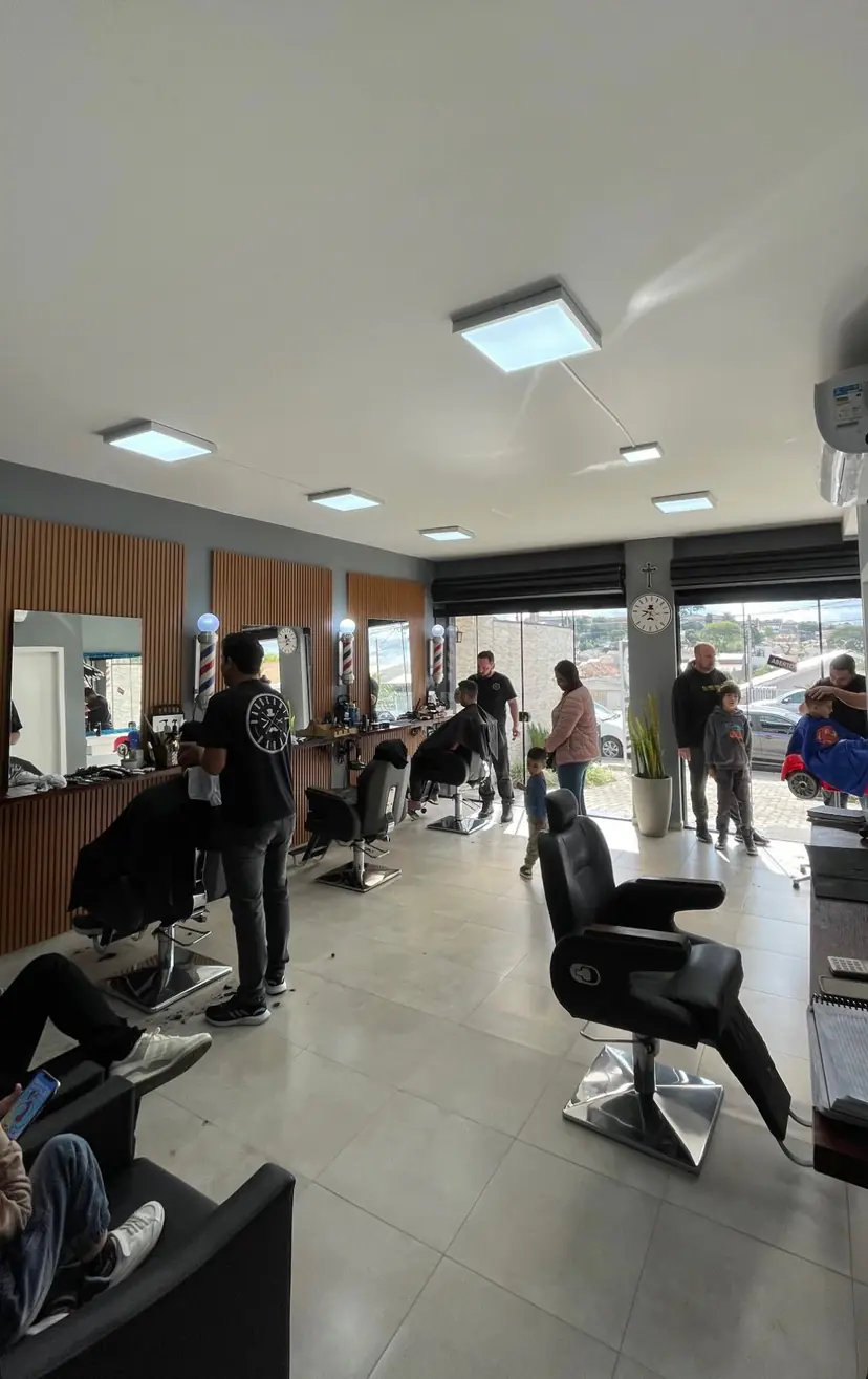 Salão com painéis de madeira, postes de barbeiro e clientes esperando